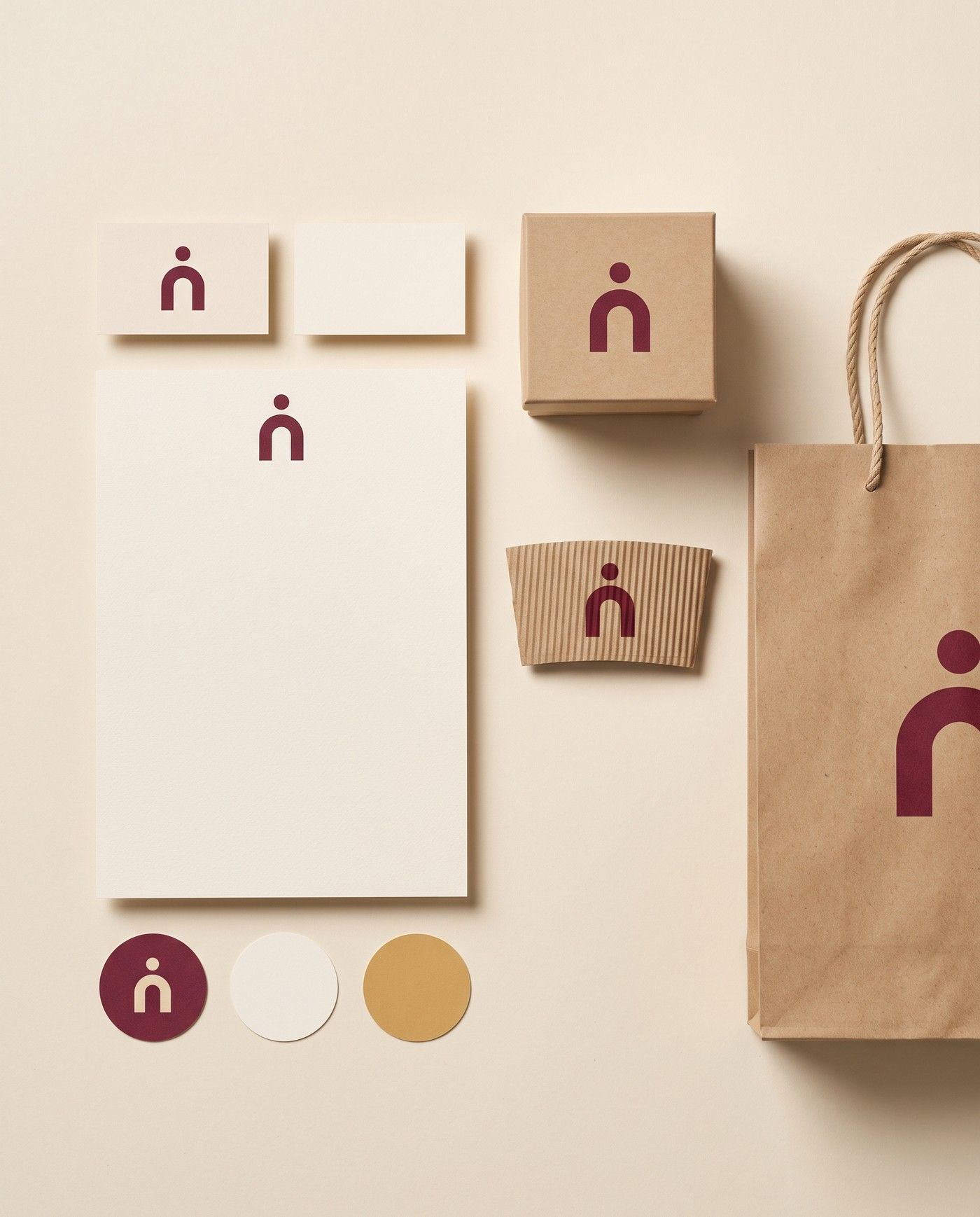 A brand identity set: business cards, letterhead, a kraft bag, a box and a cup sleeve, all with the same burgundy arch emblem, and swatches in burgundy, cream and gold.